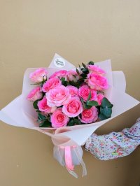 Bouquet of pink roses with greenery wrapped in pale pink paper.