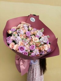 Large bouquet of peach and lavender roses with lilac stock flowers, wrapped in deep mauve paper.
