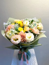 A fresh bouquet with yellow roses, peach lisianthuses, and dahlias wrapped in green paper.