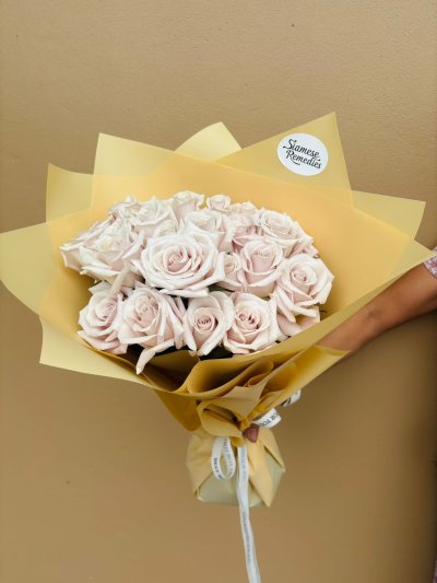 A bouquet of soft blush and ivory roses wrapped in golden honey-colored paper.