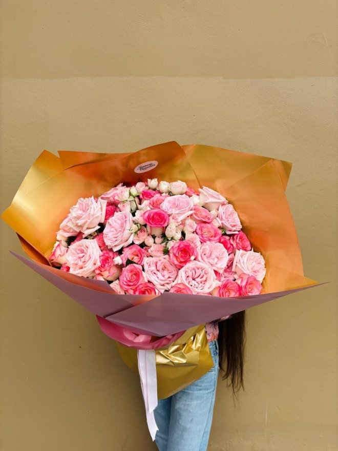A bouquet of lush pink roses wrapped in golden and pink paper.