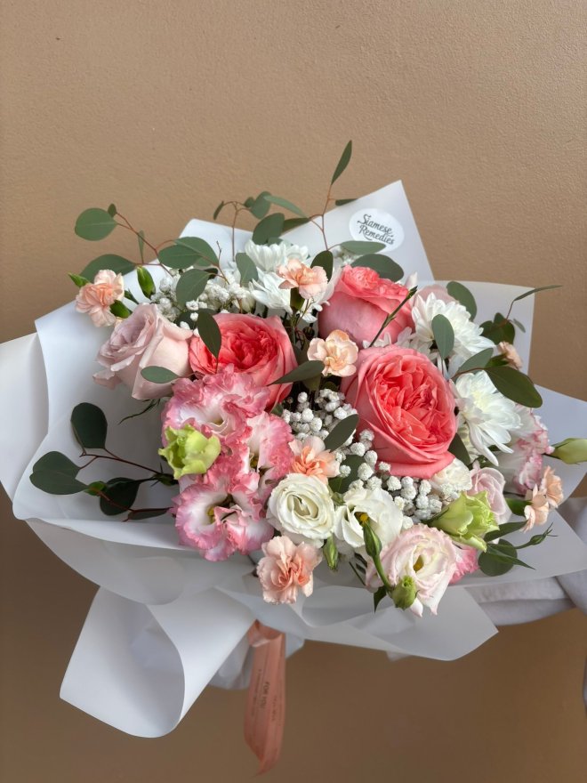 A pastel bouquet of peach roses, lisianthuses, carnations, chrysanthemums, and baby's breath wrapped in white.