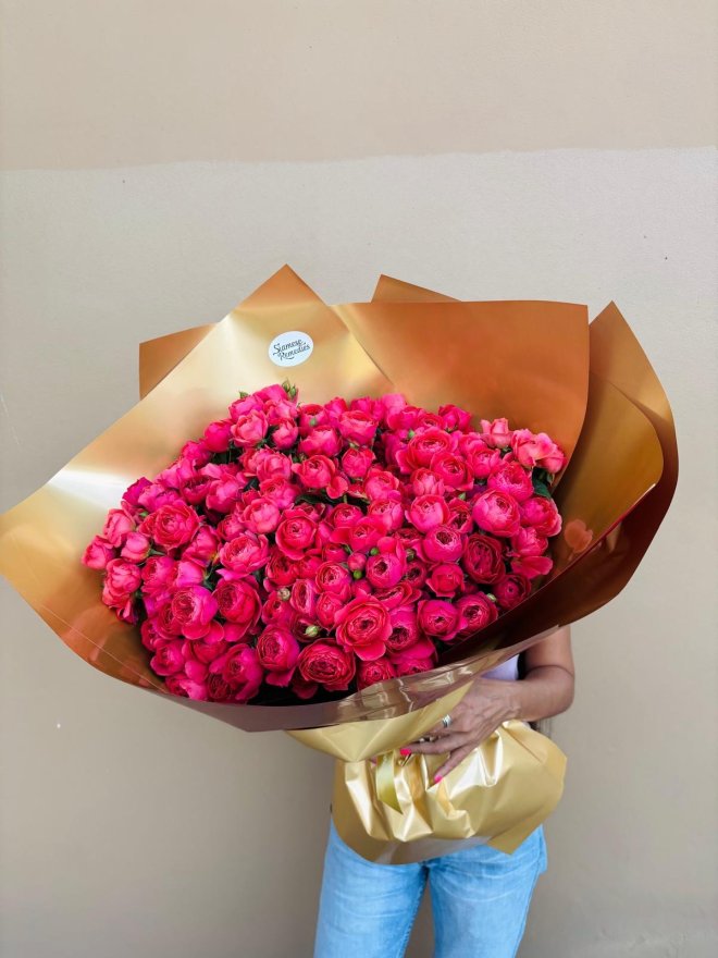A luxurious bouquet of vibrant pink roses wrapped in golden paper.