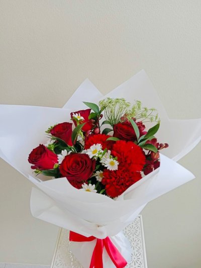 A white-wrapped bouquet with red roses, red carnations, white daisies, and greenery.