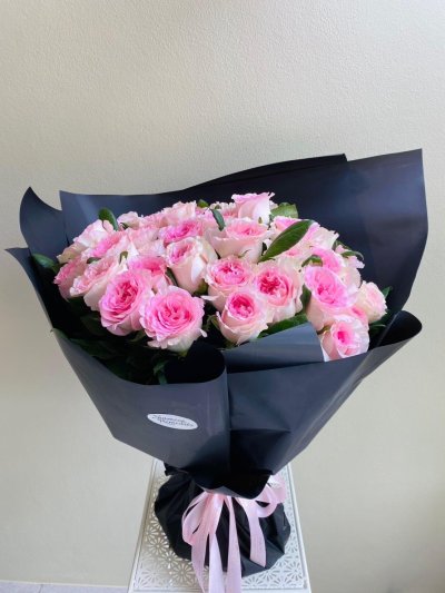 A bouquet of soft pink roses wrapped in black paper with a pink ribbon.
