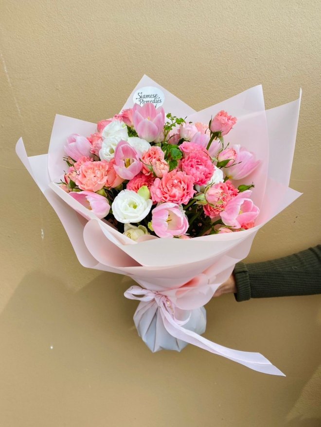 A pastel bouquet of pink tulips, white lisianthuses, and pink carnations wrapped in soft pink paper.
