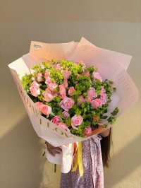 A lush bouquet of soft pink roses and vibrant green fillers wrapped in blush pink paper with a golden ribbon.