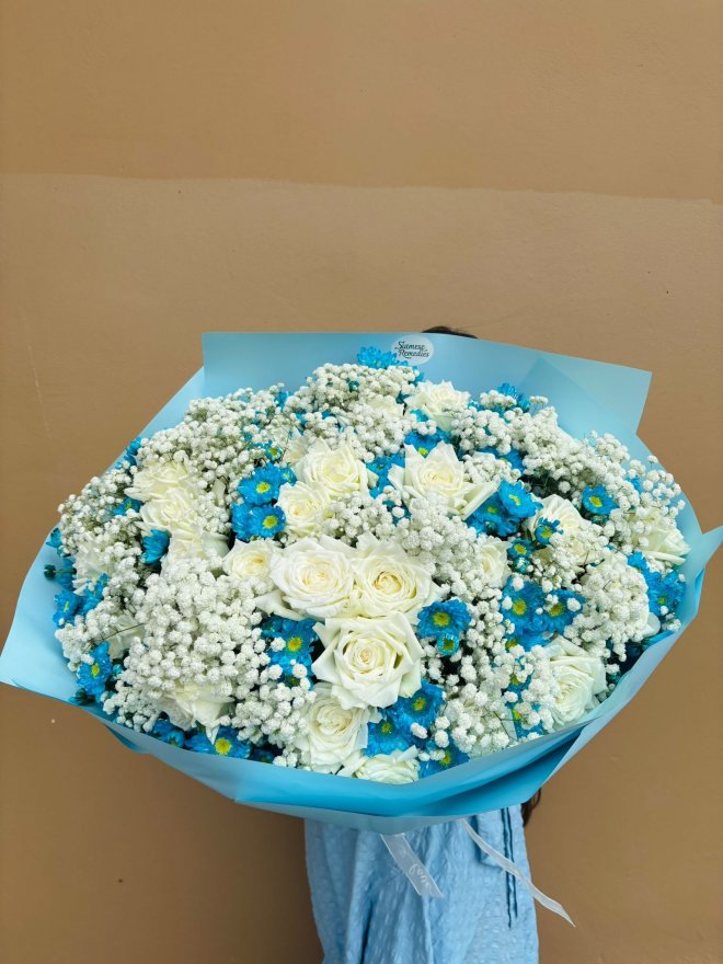 Bouquet of white roses, baby’s breath, and blue daisies wrapped in blue paper.