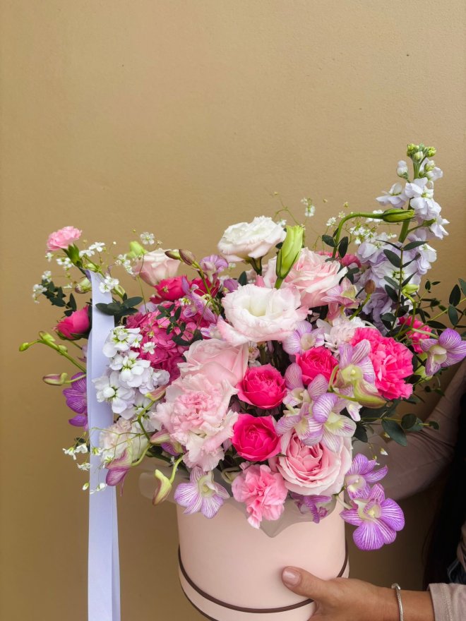 A romantic hatbox arrangement of pink roses, lisianthuses, carnations, orchids, and baby’s breath.