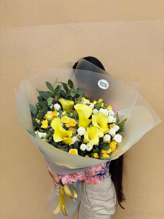 A radiant bouquet featuring yellow calla lilies, white roses, and yellow spray roses wrapped in soft paper.