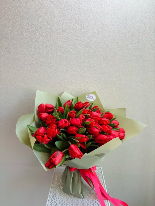 Bouquet of vibrant red tulips wrapped in matte sage green paper with a red satin ribbon