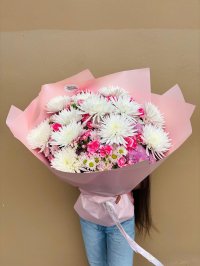 A bouquet of white spider chrysanthemums and pink blooms wrapped in blush pink paper.