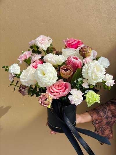 A black hat box arrangement with proteas, roses, lisianthuses, and carnations in soft pink, white, cream, and green.