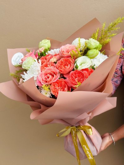 A warm-toned bouquet with coral roses, white chrysanthemums, green lisianthuses, and peach carnations.