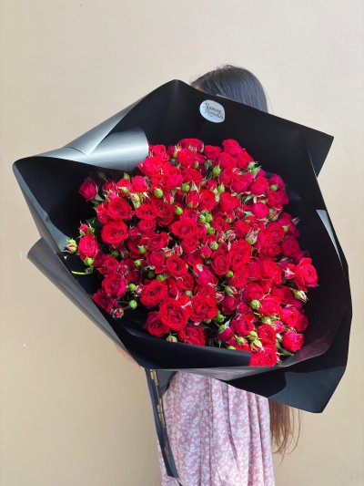 A luxurious bouquet of red spray roses wrapped in matte black paper with black and gold ribbon.