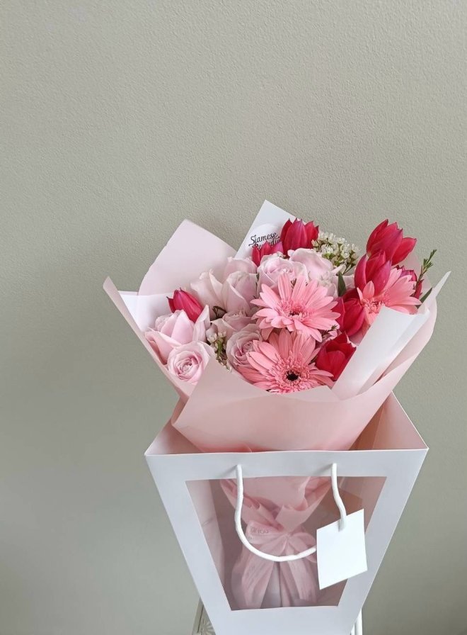 Pink bouquet with gerbera, roses, tulips and filler flowers in a transparent gift bag.