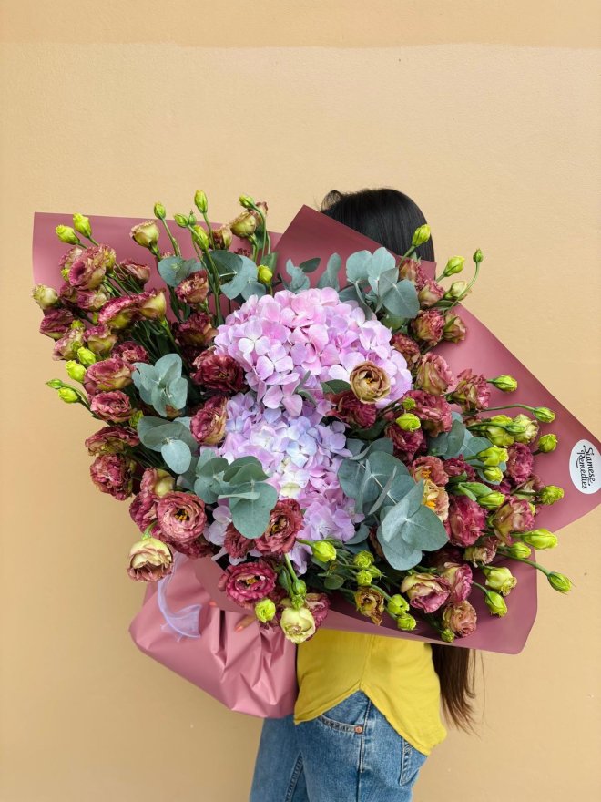 A large burgundy-wrapped bouquet of lavender hydrangeas and plum lisianthuses.