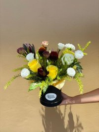 A black hat box arrangement featuring yellow and white roses, lisianthuses, and filler flowers with greenery.