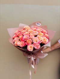 A bouquet of peach and coral roses wrapped in blush pink paper with satin ribbons.