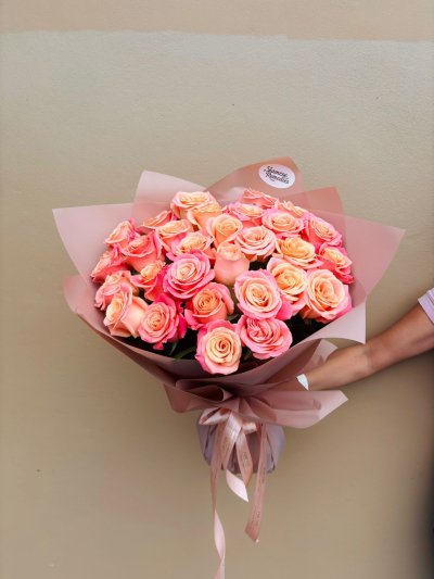 A bouquet of peach and coral roses wrapped in blush pink paper with satin ribbons.