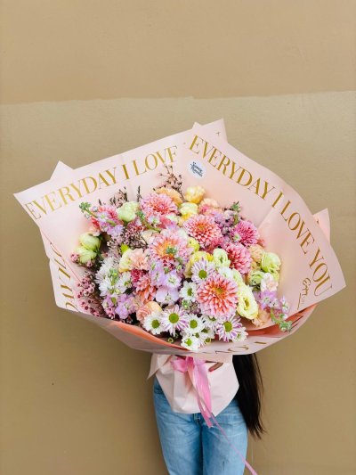 A pastel bouquet of dahlias, lisianthuses, daisies, carnations, and baby’s breath wrapped in blush pink with “Everyday I Love You” accents.