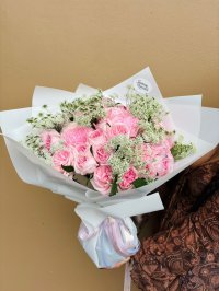 A romantic bouquet of soft pink roses, chrysanthemums, and baby’s breath wrapped in white paper.