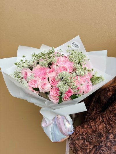 A romantic bouquet of soft pink roses, chrysanthemums, and baby’s breath wrapped in white paper.