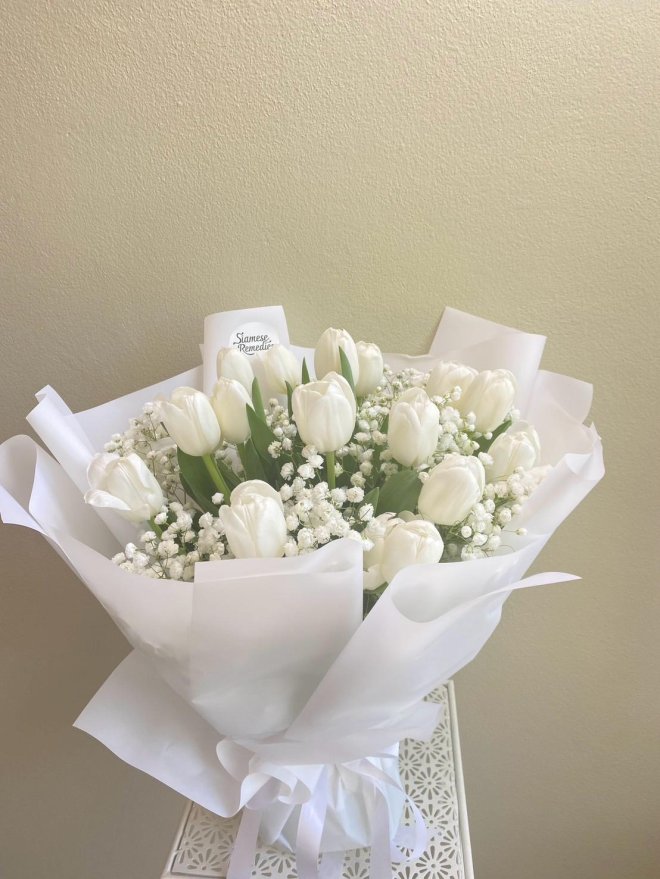 White tulip and baby’s breath bouquet wrapped in soft white paper with white satin ribbon