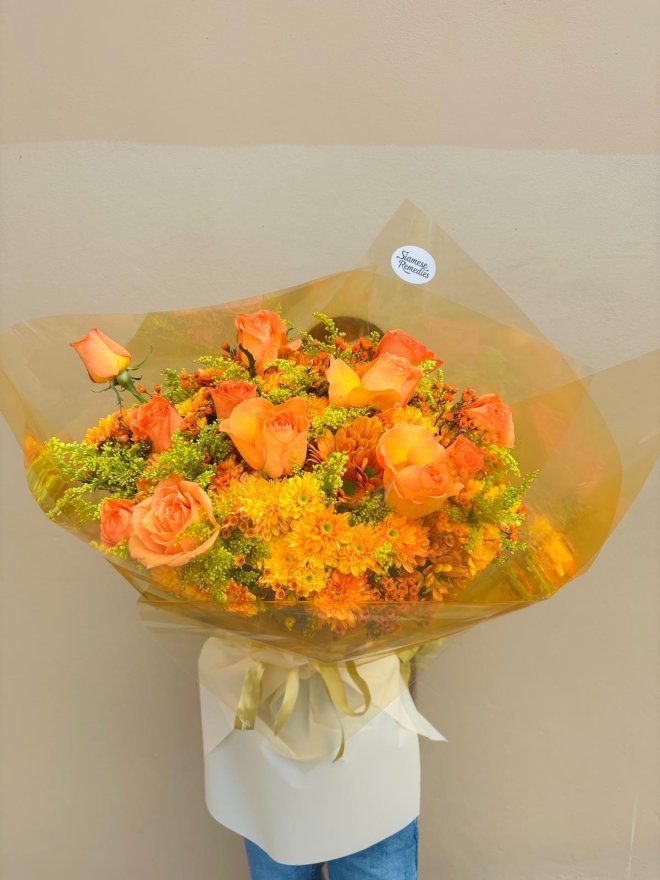 A bright bouquet of orange roses and chrysanthemums wrapped in golden paper.