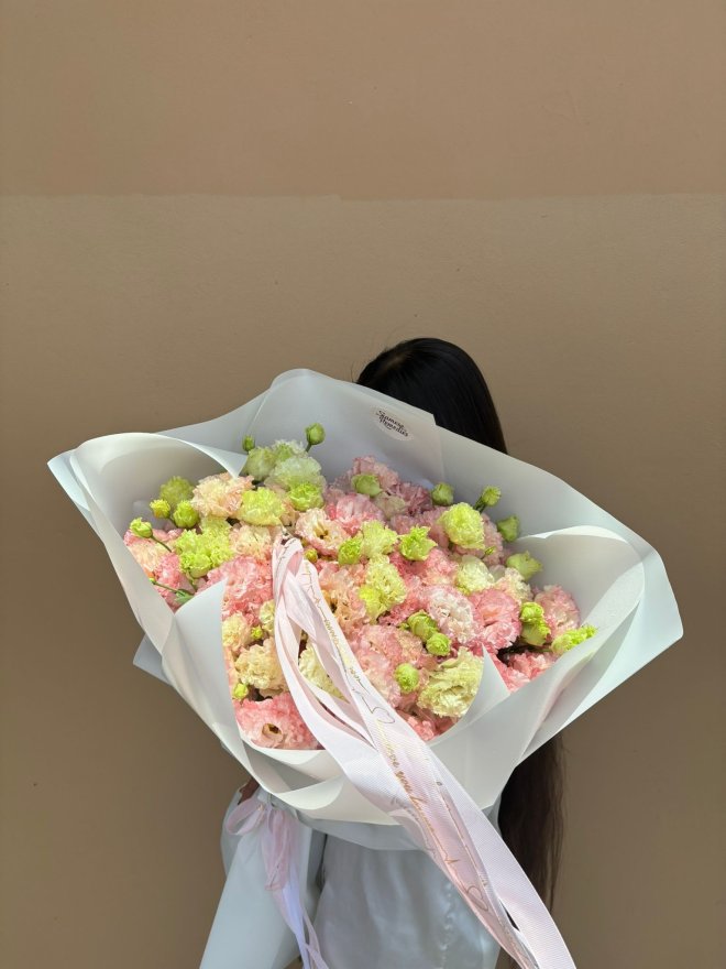 Bouquet of peach lisianthus flowers wrapped in white, held by a woman in a white blouse with long dark hair.