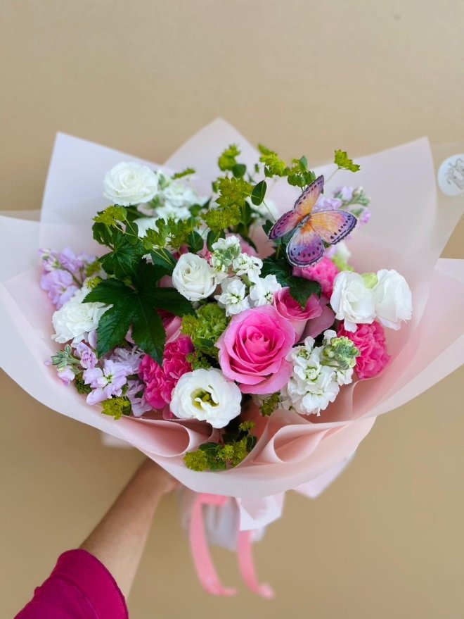 Pink and white flower bouquet with roses, lisianthus, and a butterfly accent in soft blush wrapping.