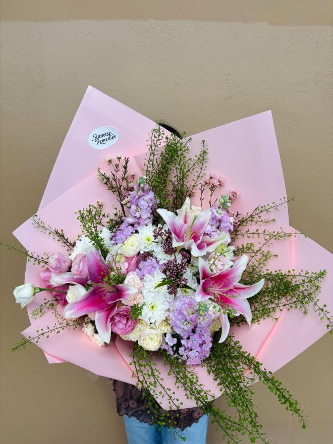 A bouquet of pink stargazer lilies, roses, hydrangeas, and greenery wrapped in blush pink paper.