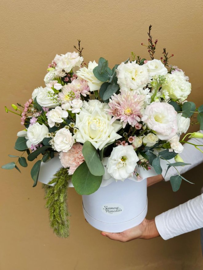 A graceful hatbox with white lisianthuses, creamy roses, pink chrysanthemums, and wax flowers.