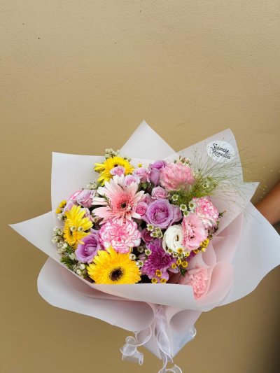 Bouquet with yellow and pink gerberas, lavender roses, pink carnations, lisianthuses, and wax flowers.
