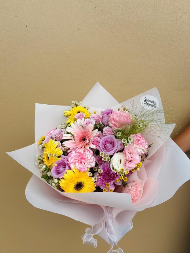 Bouquet with yellow and pink gerberas, lavender roses, pink carnations, lisianthuses, and wax flowers.