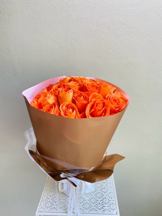 Bouquet of vibrant orange roses wrapped in caramel brown and pink paper with a white ribbon