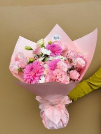 A pastel pink bouquet with dahlias, carnations, lisianthuses, and chrysanthemums wrapped in blush paper.