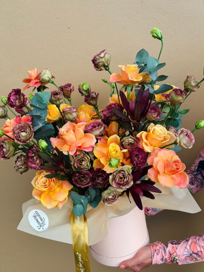 Hatbox arrangement of orange roses, burgundy lisianthuses, and eucalyptus.