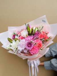 A soft pink bouquet featuring lilies, roses, carnations, lisianthuses, chrysanthemums, and baby’s breath, wrapped in blush paper.