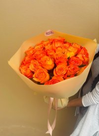 A vibrant bouquet of bright orange roses wrapped in soft peach paper.