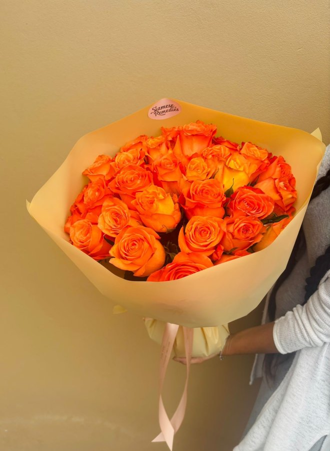 A vibrant bouquet of bright orange roses wrapped in soft peach paper.