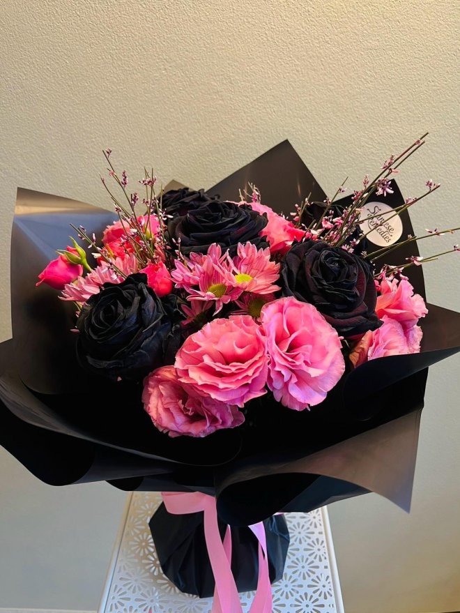 Bouquet of black roses, pink lisianthus, pink daisies, and blooming twigs wrapped in matte black paper with pink satin ribbon