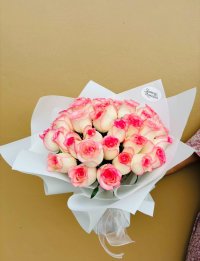 A bouquet of white roses with vivid pink-tipped petals, wrapped in white paper.
