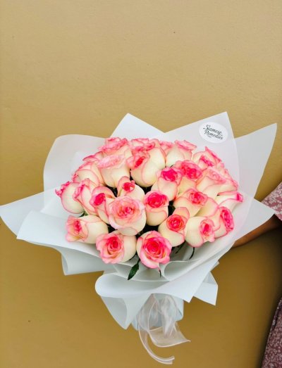 A bouquet of white roses with vivid pink-tipped petals, wrapped in white paper.