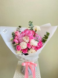 Bouquet of pink roses, white carnations, hydrangeas, lisianthus, and eucalyptus wrapped in white paper with a pink satin ribbon