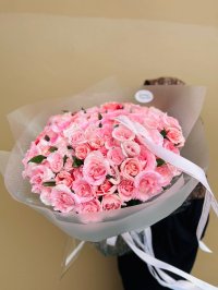 A large bouquet of soft pink garden roses wrapped in translucent white paper with white ribbons.