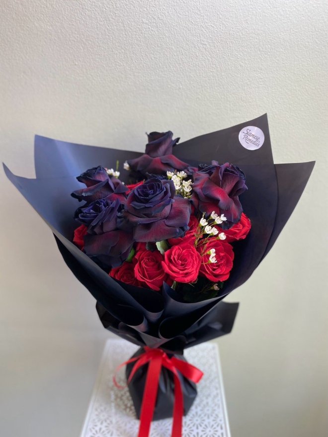 Bouquet of black and red roses wrapped in matte black paper with a red ribbon.