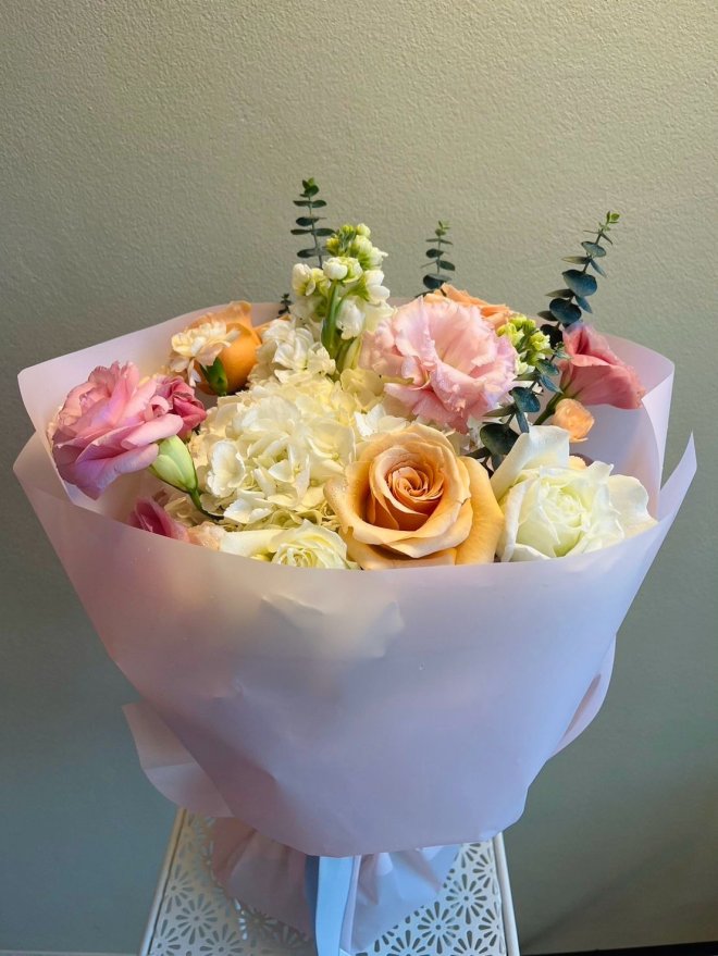 Elegant bouquet of peach and white roses, blush lisianthus, white hydrangeas, and eucalyptus wrapped in pale pink paper.
