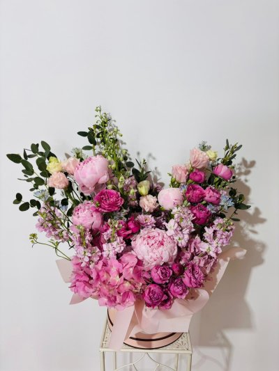 A lavish pink hatbox bouquet with peonies, roses, lisianthuses, carnations, hydrangeas, and stock flowers.