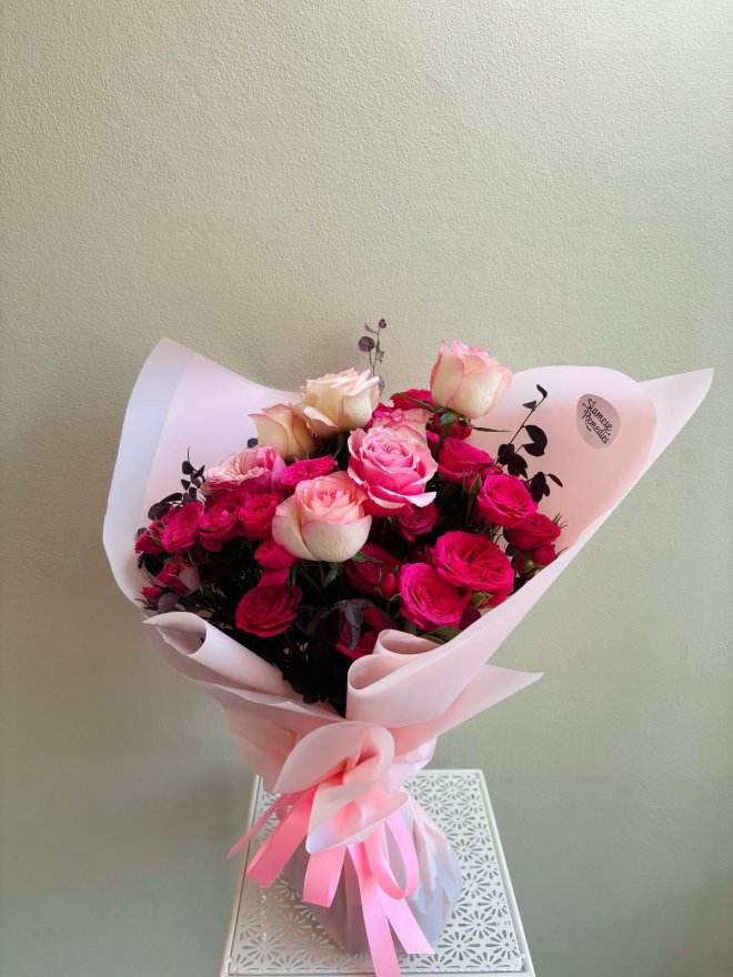 Bouquet of blush and deep pink roses wrapped in soft pink paper with layered satin ribbon